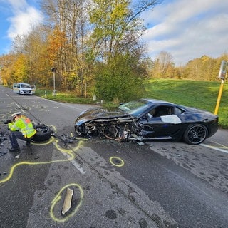 Ein schwer beschädigter Ferrari steht nach einem Unfall mit einem Lieferwagen auf einer Straße.