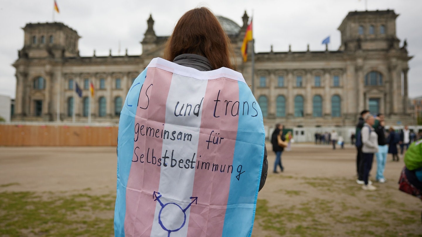 Eine Teilnehmerin steht bei einer Protestveranstaltung gegen das Selbstbestimmungsgesetz von Frauengruppen mit einer Trans-Pride-Flagge vor dem Bundestag.