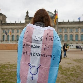 Eine Teilnehmerin steht bei einer Protestveranstaltung gegen das Selbstbestimmungsgesetz von Frauengruppen mit einer Trans-Pride-Flagge vor dem Bundestag.