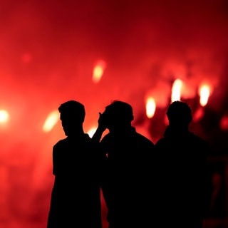 Menschen vor rotem Bengalo-Feuer: Pyrotechnik vor der Arena in Trier sorgt für späten Spielstart im Basketball 2. Liga.