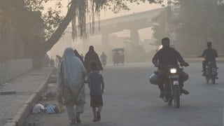 Eine Frau und ein Kind an ihrer Hand laufen durch einen versmogten Straßenzug in Pakistan.