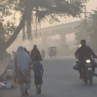 Eine Frau und ein Kind an ihrer Hand laufen durch einen versmogten Straßenzug in Pakistan.