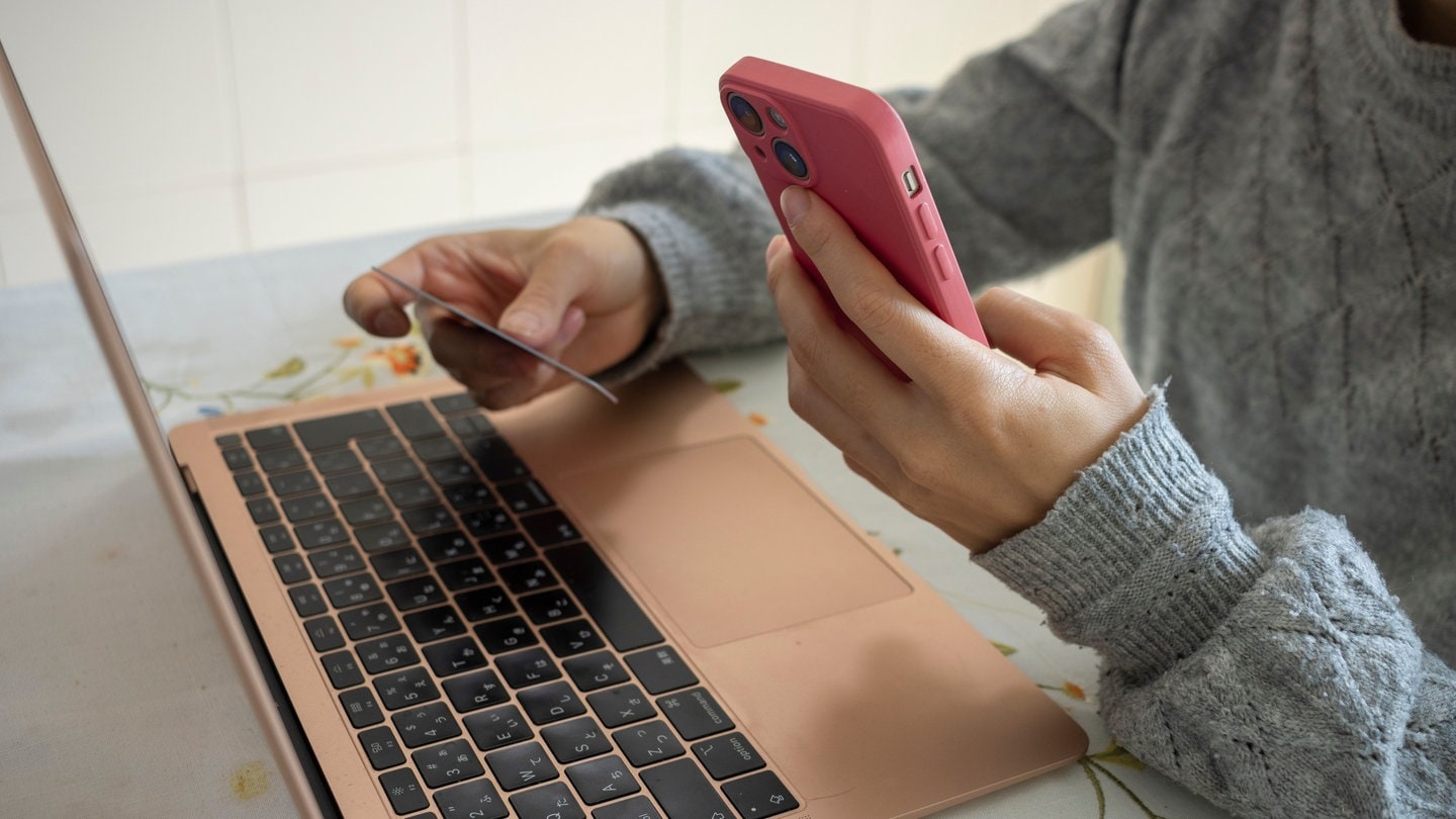 Frau mit Handy und Laptop schließt einen Online-Einkauf ab.