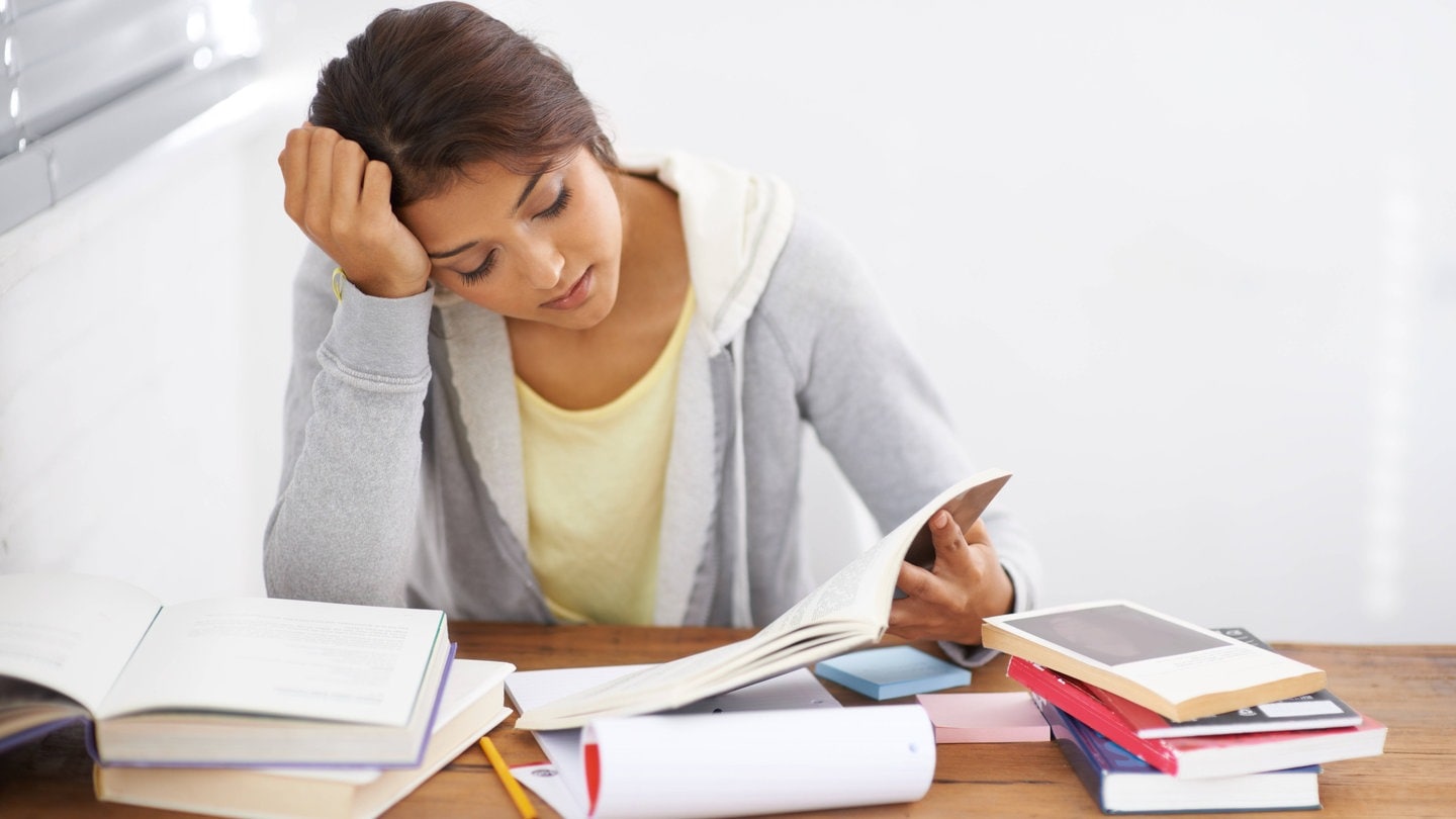 Eine Schülerin sitzt an einem Schreibtisch und lernt, vor ihr liegen Hefte und Bücher.