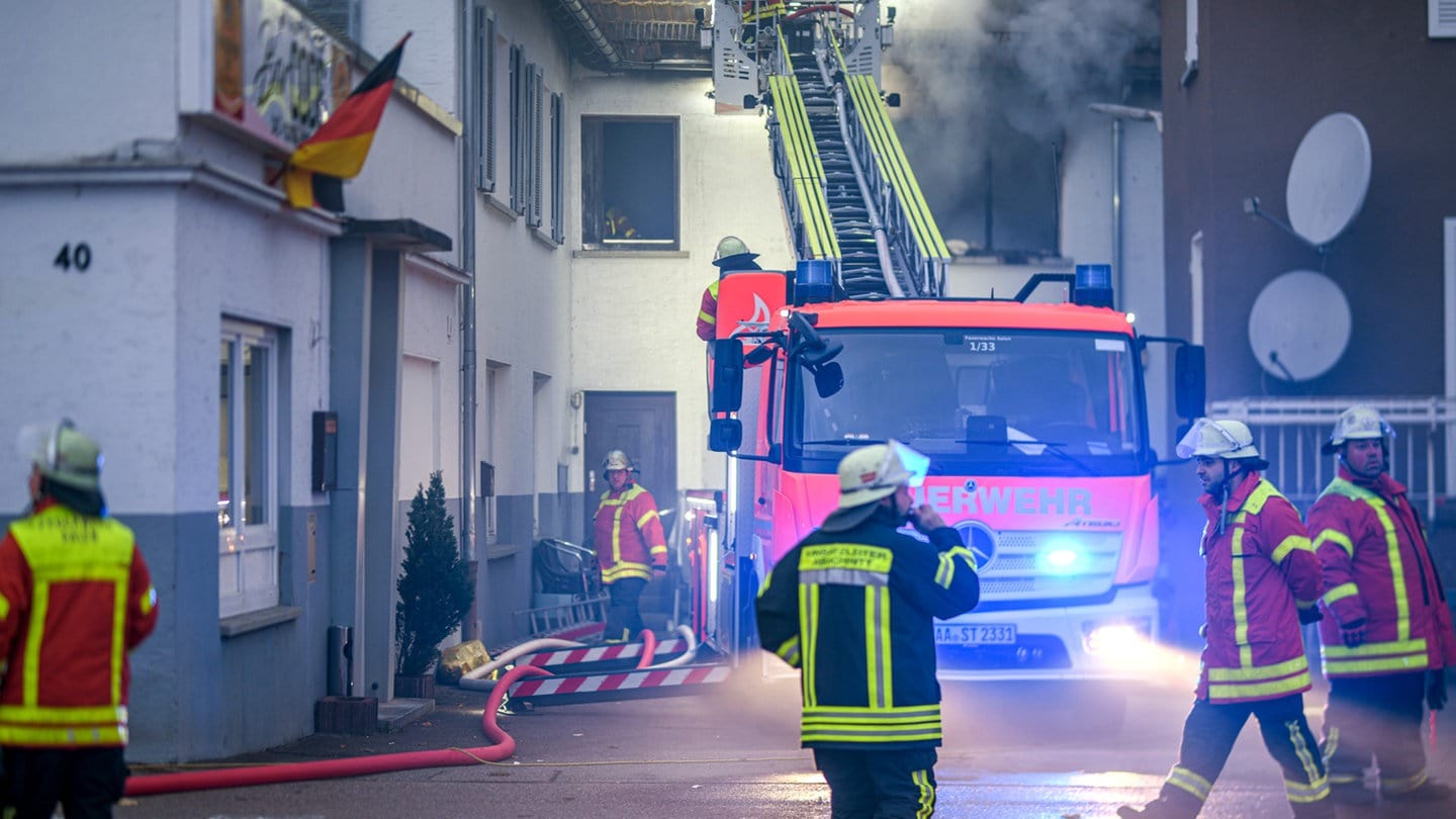 Feuerwehrleute löschen einen Brand in einer Obdachlosenunterkunft. Bei dem Feuer wurden vier Personen verletzt. 14 weitere mussten von Einsatzkräften betreut und untersucht werden.