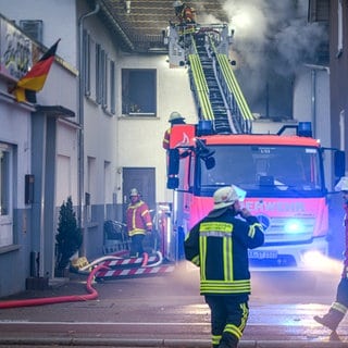 Feuerwehrleute löschen einen Brand in einer Obdachlosenunterkunft. Bei dem Feuer wurden vier Personen verletzt. 14 weitere mussten von Einsatzkräften betreut und untersucht werden.