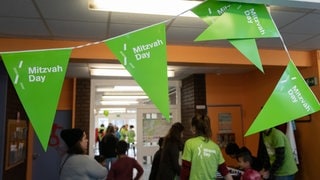 Grüne Fahnen mit der Aufschrift "Mitzvah Day" hängen in einem Gang. (Archivbild)