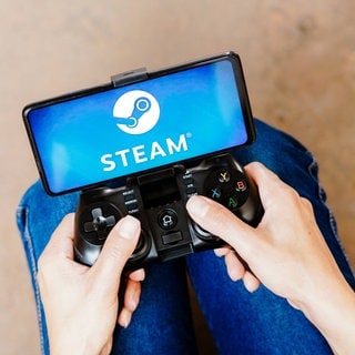 Eine Person hält einen Controller mit Handy auf dem das Steam-Logo erscheint