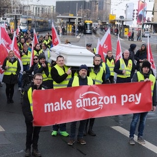 Teilnehmer einer Demonstration der Gewerkschaft Verdi laufen am Black Friday 2022 mit Fahnen und tragen ein Transparent mit der Aufschrift "Make Amazon pay" sowie einen Sarg.