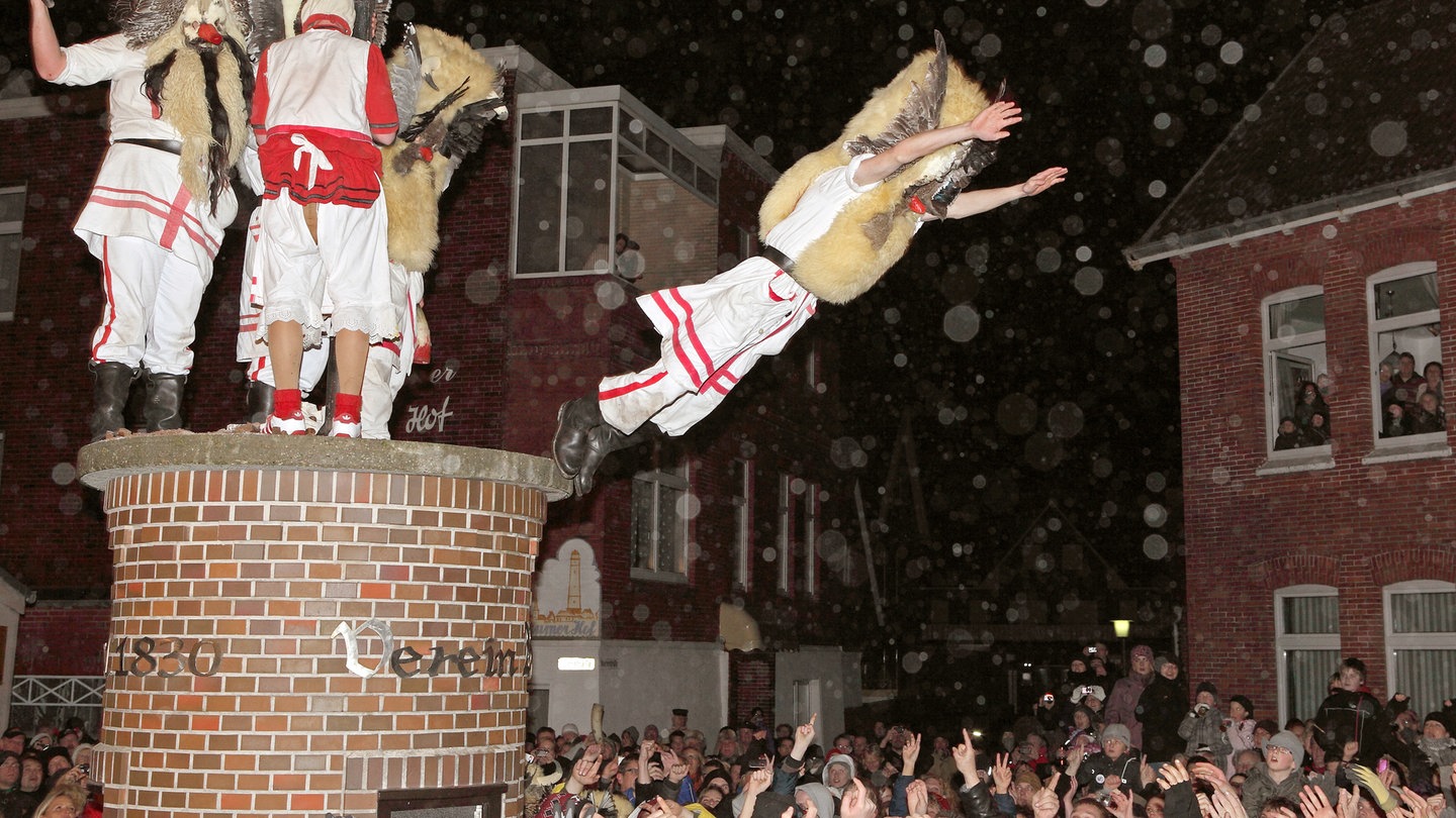 Tradition: Männer verkleidet als Klaasohms springen in Borkum von einer Litfaßsäule in die Menge.