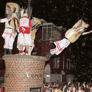 Tradition: Männer verkleidet als Klaasohms springen in Borkum von einer Litfaßsäule in die Menge.