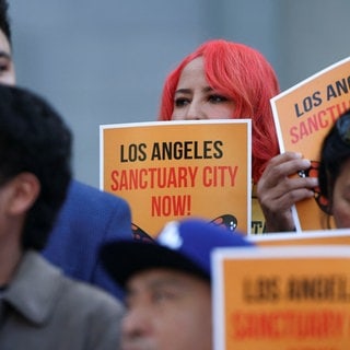 Menschen halten Schilder, auf denen "Los Angeles Sanctuary City Now!" steht