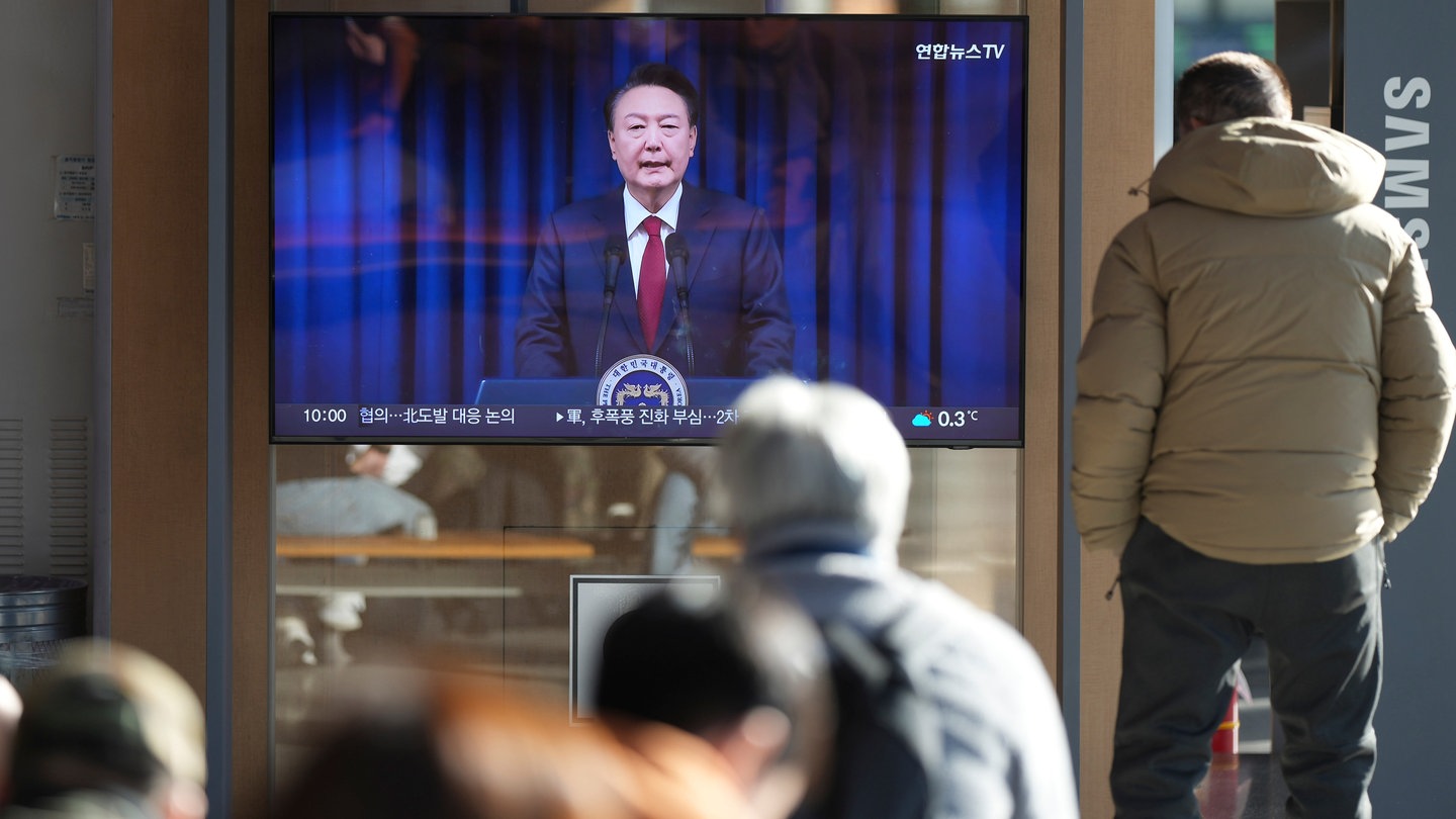 Menschen in Südkorea schauen auf einen Fernsehbildschirm, der die Live-Übertragung der Ankündigung des südkoreanischen Präsidenten Yoon Suk Yeol im Bahnhof von Seoul zeigt.