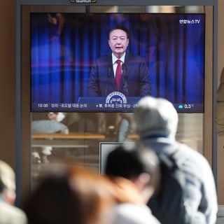 Menschen in Südkorea schauen auf einen Fernsehbildschirm, der die Live-Übertragung der Ankündigung des südkoreanischen Präsidenten Yoon Suk Yeol im Bahnhof von Seoul zeigt.