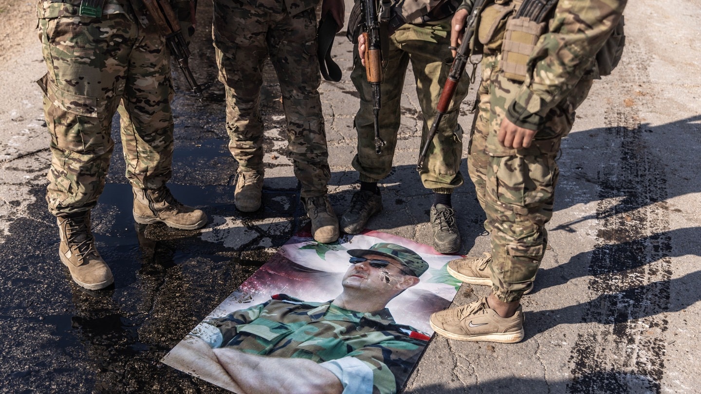 Bewaffnete syrische Oppositionskämpfer stellen ihre Füße auf ein Plakat mit einem Foto des syrischen Präsidenten Baschar al-Assad. Er ist nach Russland geflüchtet.