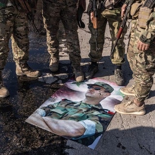 Bewaffnete syrische Oppositionskämpfer stellen ihre Füße auf ein Plakat mit einem Foto des syrischen Präsidenten Baschar al-Assad. Er ist nach Russland geflüchtet.