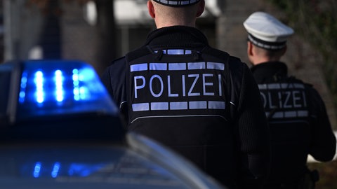 Das Logo der Polizei auf der Dienstkleidung von Polizisten die vor einem Blaulicht stehen. Am Sonntag soll in Dietingen ein 14-Jähriger auf einen 12-Jährigen geschossen haben. Jetzt sitzt er in Untersuchungshaft, die Polizei ermittelt.