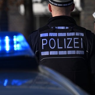 Das Logo der Polizei auf der Dienstkleidung von Polizisten die vor einem Blaulicht stehen. Am Sonntag soll in Dietingen ein 14-Jähriger auf einen 12-Jährigen geschossen haben. Jetzt sitzt er in Untersuchungshaft, die Polizei ermittelt.