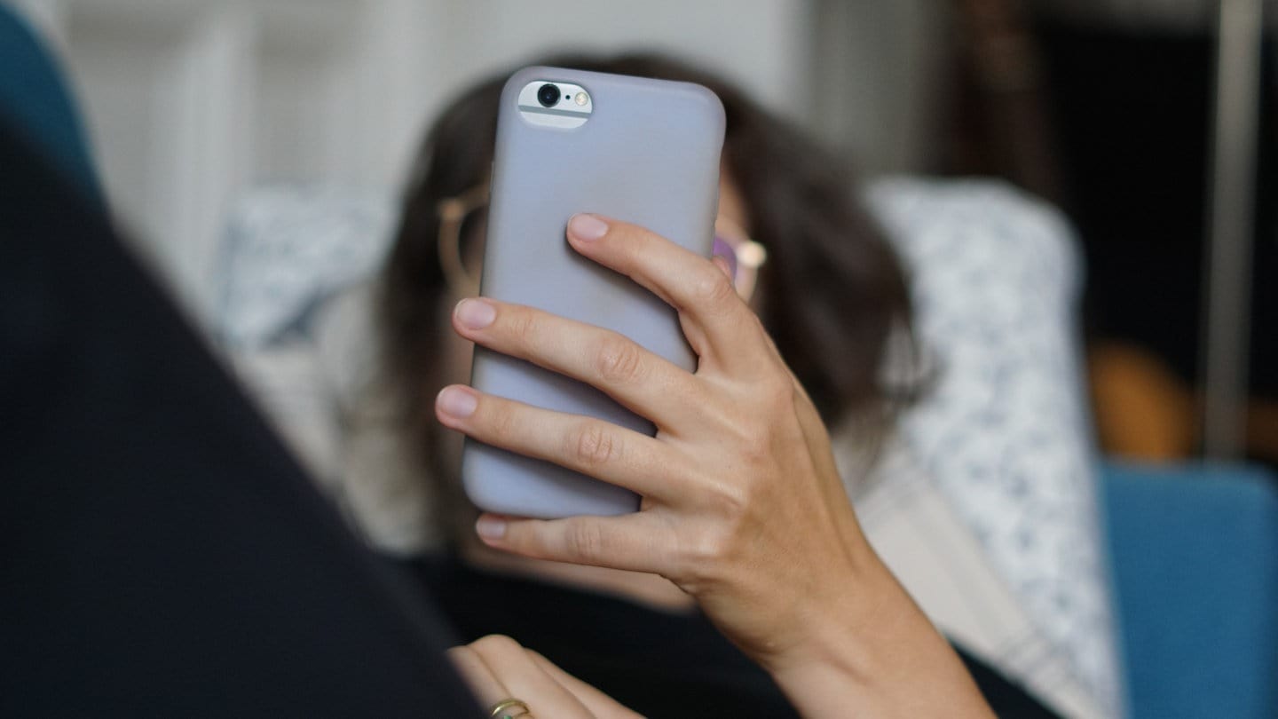 Eine Frau liegt auf einem Sofa und schaut ihr Handy. Viele Menschen schreien ihre Technik wie Handy oder Laptop an, wenn etwas nicht funktioniert.