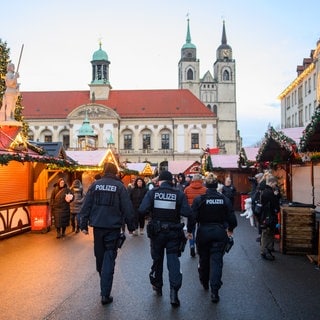 Polizisten und Passanten gehen über den geschlossenen Weihnachtsmarkt in Magdeburg. Nach der Attacke am 20. Dezember gibt es Kritik am Sicherheitskonzept auf dem Weihnachtsmarkt.