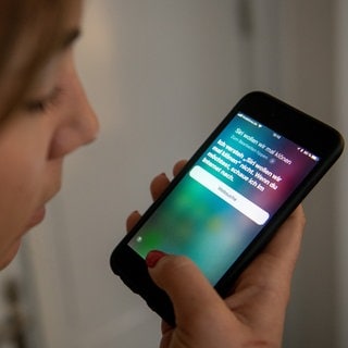 Eine junge Frau bedient auf einem iPhone die Spracherkennung des Apple-Programms Siri. 