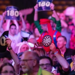 Zuschauer halten Dart-Scheiben mit der Zahl 180 in die Höhe. Der Hauptsponsor der Darts-WM hat ordentlich Cash locker gemacht. Das Geld geht an eine britische Prostatakrebs-Vorsorge-Organisation.