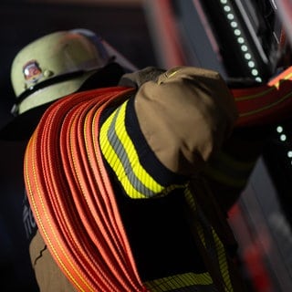 Eine Person mit Feuerwehr-Uniform und einem Wasserschlauch um die Schulter gewickelt.