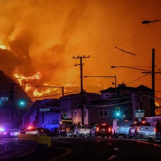 Feuer ist am Berg über Malibu zu sehen, während sich Autos auf der Straße davor stauen