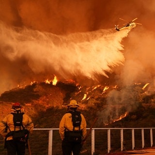 Feuerwehrleute beobachten, wie Löschwasser auf das Palisades-Feuer im Mandeville Canyon Angeles geworfen wird.