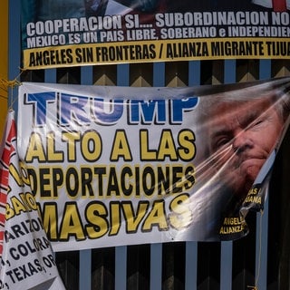 Ein Mitglied der Menschenrechtsorganisation "Engel ohne Grenzen" ("Angels Without Borders") platziert ein Schild mit der Aufschrift "Trump, stoppen Sie Massenabschiebungen" während eines Protestes gegen den designierten US-Präsidenten Trump am Vorabend seiner Amtseinführung am Grenzzaun, der Mexiko von den USA trennt.