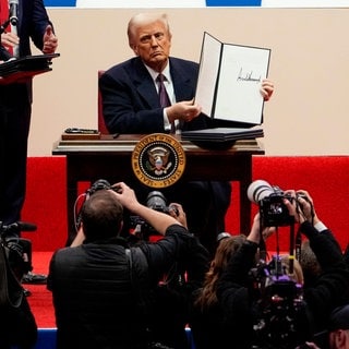 US-Präsident Donald Trump unterzeichnet auf der Bühne während der Inaugurationsparade in der Capital One Arena in Washington D.C. eine Reihe von Executive Orders - Dekrete.