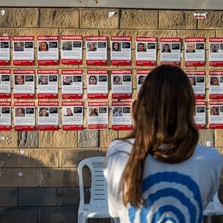 Eine Frau fotografiert eine Wand, die mit Bildern der Geislen beklebt ist. Am Samstag sollen die nächsten Geiseln freikommen. Das hat die Hamas bestätigt.