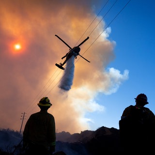 Ein Löschhubschrauber ist im Einsatz. Feuerwehrleute blicken zu ihm auf.