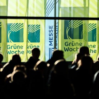 Besucher gehen in einer Halle vor Fahnen der "Grünen Woche".