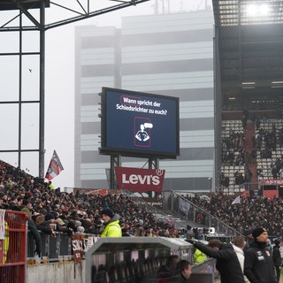 In einem Bundesligastadion wird vor Spielbeginn der Ablauf der Verkündung des Schiedsrichters zum VAR-Beweis erklärt. Schiedsrichter erklären den Zuschauern jeden wichtigen VAR-Eingriff per Lautsprecher-Durchsage.