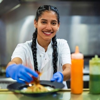 Eine junge Frau legt einen Teller mit Essen auf dem Pass in einem Restaurant ab.