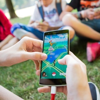 Jugendliche spielen in einem Park Pokémon Go auf ihren Smartphones. Das Spiel soll jetzt verkauft werden.