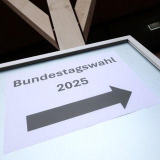 Ein Hinweisschild mit der Aufschrift "Bundestagswahl 2025" steht vor einem Wahllokal.