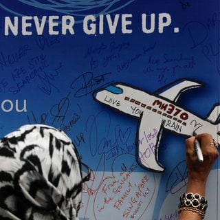 Eine Frau schreibt während einer Gedenkveranstaltung zum Flug MH370 eine Nachricht auf ein Banner. - Jetzt startet eine neue Suchaktion nach dem verschollenen Flugzeug.