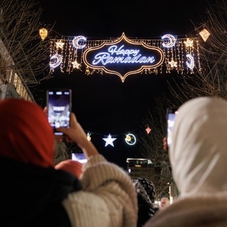 Zwei Frauen fotografieren mit ihren Handys die "Happy Ramadan"-Beleuchtung in Frankfurt am Main