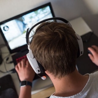 Ein Mann sitzt am mit einem Headset vor einem Laptop und spielt ein Online-Computerspiel. - Die WHO warnt vor Hoerschäden durch Videospiele 