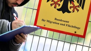 Ein Mann füllt ein Formular aus neben einem Schild vom Bundesamt für Migration und Flüchtlinge