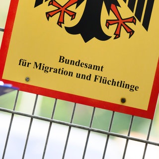 Ein Mann füllt ein Formular aus neben einem Schild vom Bundesamt für Migration und Flüchtlinge