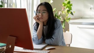 Eine junge Frau sitzt zu Hause an ihrem Computer und arbeitet (Symbolbild)