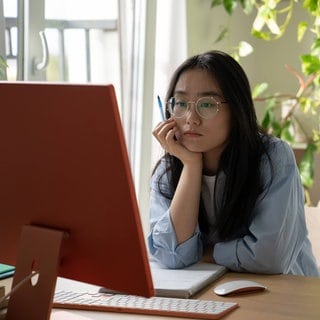 Eine junge Frau sitzt zu Hause an ihrem Computer und arbeitet (Symbolbild)