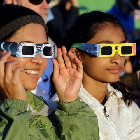 Drei Frauen mit einer speziellen Brille für eine Sonnenfinsternis. Ende März kannst du eine Sonnenfinsternis über Deutschland beobachten.