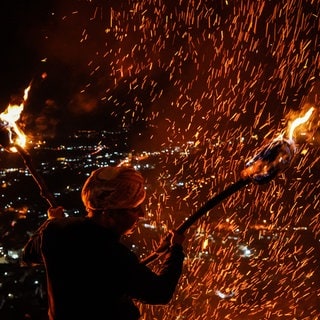 Ein irakisch-kurdischer Mann steht während der Feierlichkeiten zum kurdischen Neujahrsfest Newroz auf einem Berg und hält Fackeln in der Hand. Newroz wird 2025 am 20. März gefeiert.