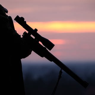 Ein Jäger hält sein Gewehr in der Abenddämmerung
