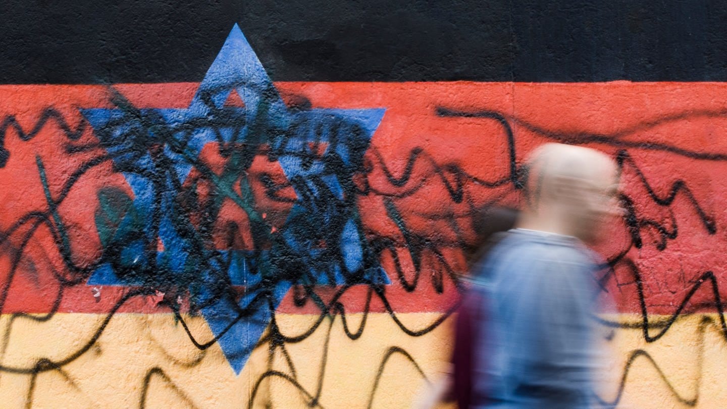 Beschmiertes Wandbild, das die schwarz-rot-goldene Deutschlandfahne mit einem blauem Davidstern zeigt