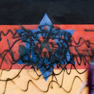 Beschmiertes Wandbild, das die schwarz-rot-goldene Deutschlandfahne mit einem blauem Davidstern zeigt